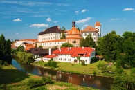 Panorama einer historischen Stadt mit Fluss und grüner Landschaft bei Sonnenschein.