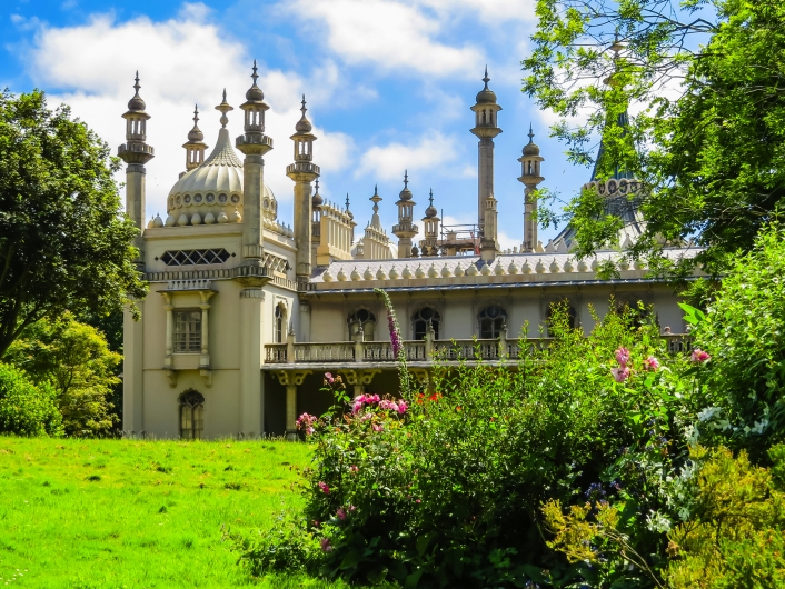 Historisches Gebäude mit Kuppeln und Türmen hinter grüner Wiese und Bäumen.