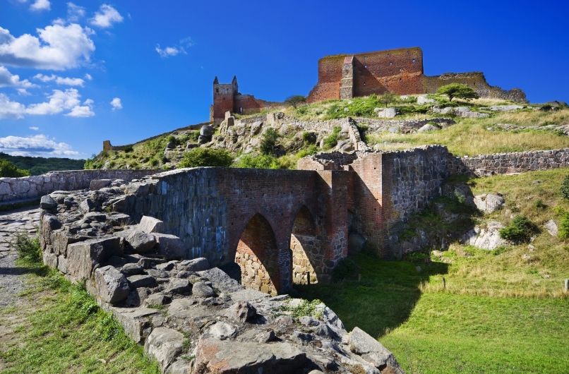 Ruine einer mittelalterlichen Burg auf einem Hügel unter blauem Himmel.