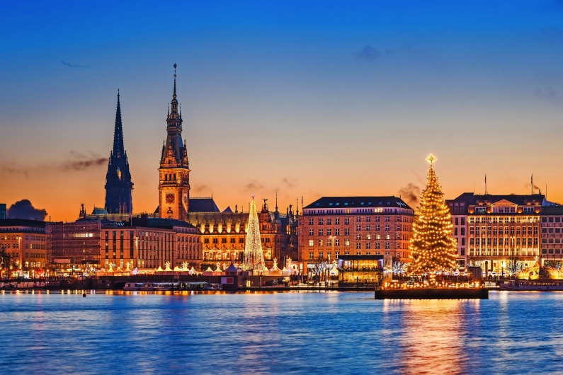 Abendliche Skyline von Hamburg mit Weihnachtsbaum und Lichtern am Wasser.