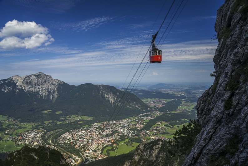 Seilbahn mit roter Gondel über einer Alpenlandschaft, Blick auf Täler und Berge bei klarem Himmel.
