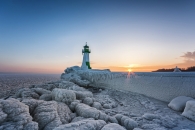 Vereister Leuchtturm bei Sonnenuntergang am Meer.
