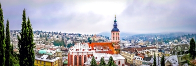 Panorama einer schneebedeckten Stadt mit Kirche und Hügeln im Hintergrund.