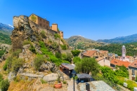Burg auf Felsen über einem Dorf in einer bergigen Landschaft unter klarem Himmel.