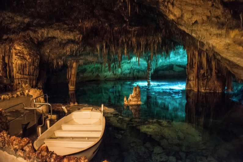 Boot in einer beleuchteten Höhle mit Stalagmiten und Stalaktiten.
