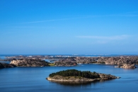 Insel mit Bäumen in einem ruhigen, blauen Meer unter klarem Himmel.