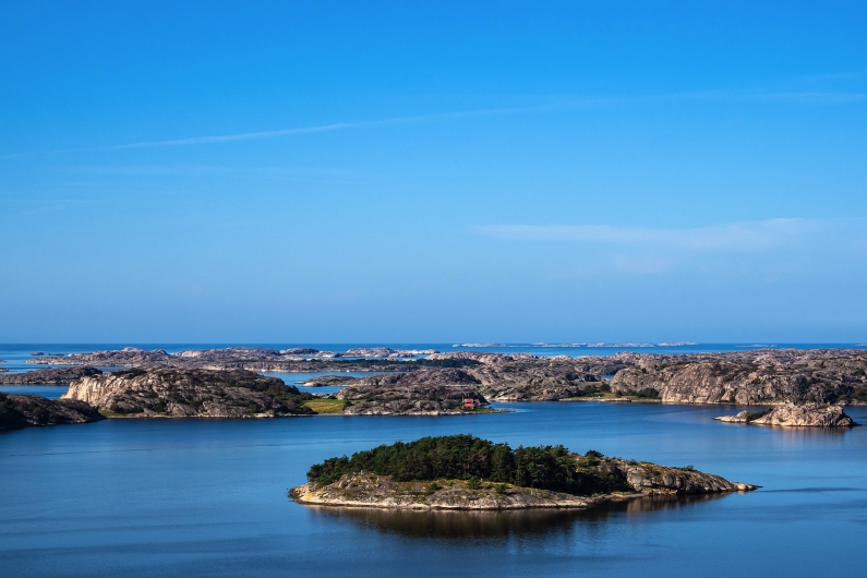 Insel mit Bäumen in einem ruhigen, blauen Meer unter klarem Himmel.