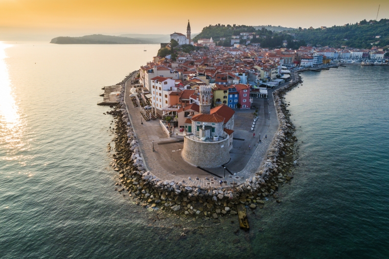 Luftaufnahme der Halbinsel mit bunten Gebäuden und einer Kirche am Meer.