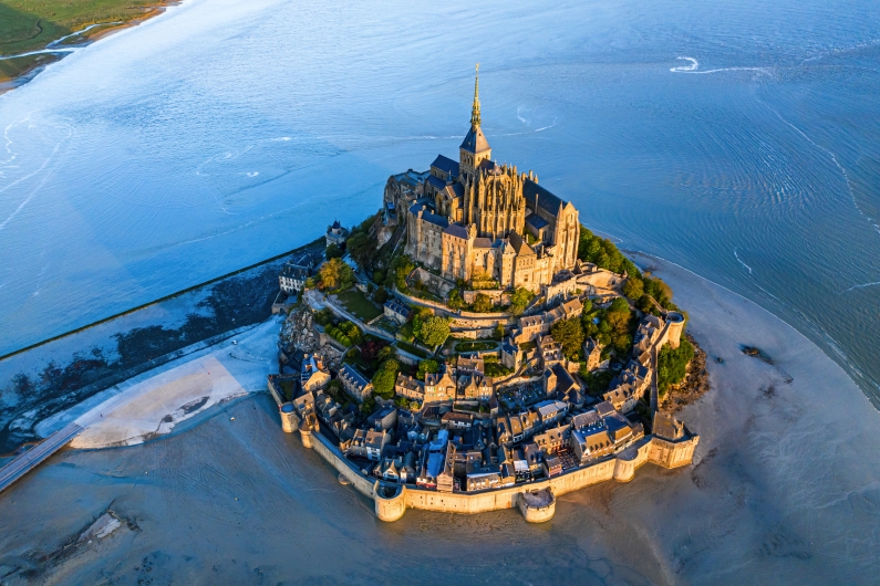 Luftaufnahme von Mont Saint-Michel bei Ebbe, umgeben von Sand und Meer.