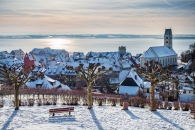 Verschneite Stadt mit Kirche und Blick auf einen See im Hintergrund.