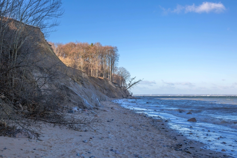 Küste mit steilen Klippen und Bäumen am Meer bei klarem Himmel.