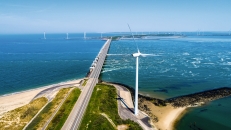 Luftaufnahme von Deichstraße mit Windkraftanlagen am Meer.