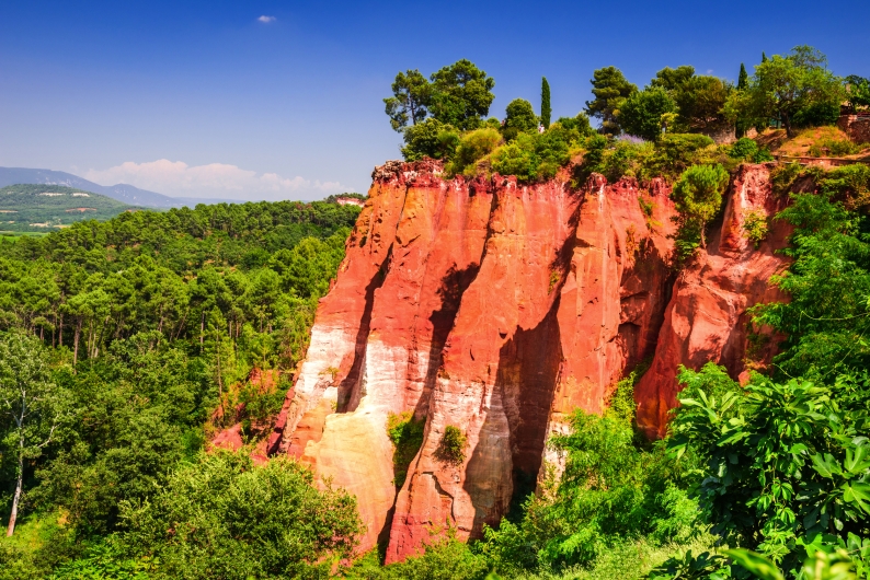 Ockerfelsen in Roussillon, Frankreich mit Bäumen und blauem Himmel.
