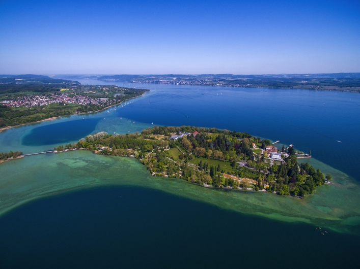 Luftaufnahme einer grünen Insel in einem blauen See bei klarem Himmel.
