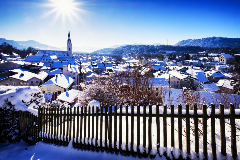 Verschneite Stadtlandschaft mit Kirche und Bergen im Hintergrund.