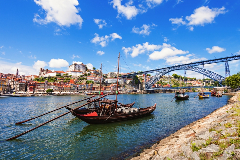 Boote auf einem Fluss vor einer Brücke in einer Stadtlandschaft mit blauem Himmel.