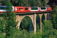 Roter Glacier Express auf steinernes Viadukt umgeben von Wald.