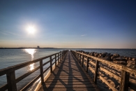 Hölzerne Promenade zum Meer bei Sonnenuntergang, sonniger Himmel, ruhiges Wasser.