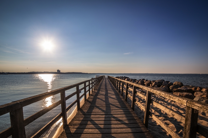 Hölzerne Promenade zum Meer bei Sonnenuntergang, sonniger Himmel, ruhiges Wasser.