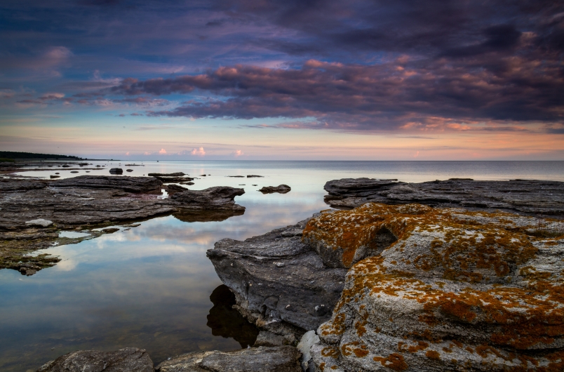 Steinige Küste bei Sonnenuntergang mit Wolken und ruhigem Wasser.