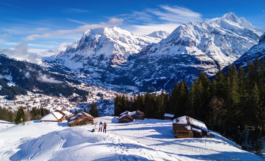 Winterlandschaft mit Berghütten, schneebedeckten Bergen und blauen Himmel.