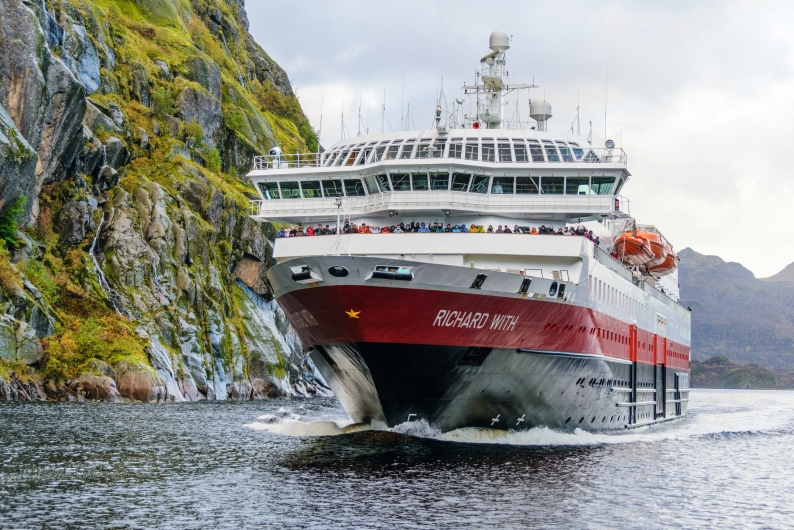 Passagierschiff im schmalen Fjord zwischen steilen Felswänden.