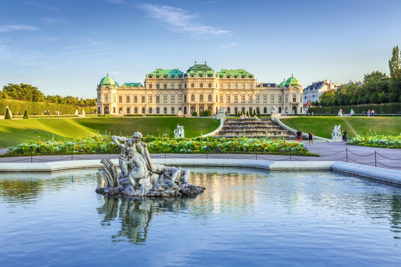 Barockschloss mit Garten und Teich im Vordergrund bei sonnigem Himmel.