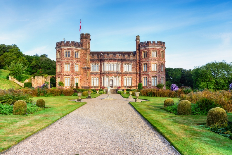 Altes Schloss mit Garten und blauen Himmel im Hintergrund.