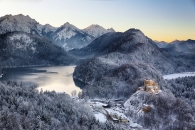 Winterliche Berglandschaft mit Schloss und See bei Sonnenuntergang.
