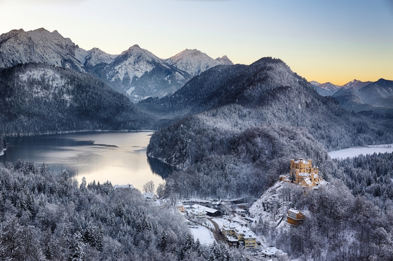 Winterliche Berglandschaft mit Schloss und See bei Sonnenuntergang.