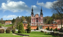 Barockkirche in einer grünen Parklandschaft unter blauem Himmel mit Wolken.