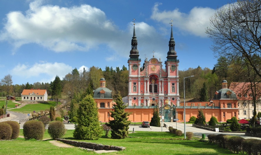 Barockkirche in einer grünen Parklandschaft unter blauem Himmel mit Wolken.