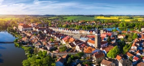 Luftaufnahme einer historischen Stadt mit Kirche und Fluss im Sonnenlicht.