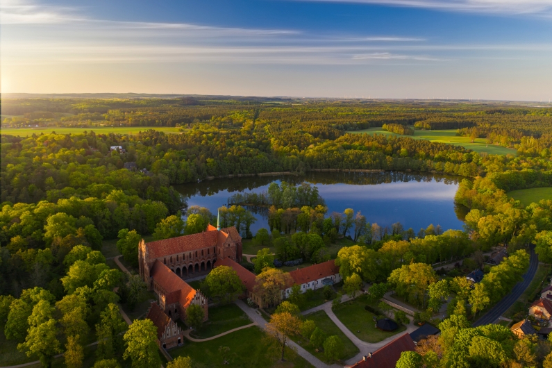 Luftaufnahme eines Backsteingebäudes neben einem See in einer grünen Landschaft.