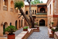 Innenhof mit Baum, Topfpflanzen und antikem Gebäude in warmen Farbtönen.