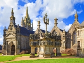 Historischer Steinbau mit verzierten Skulpturen, Kirche im Hintergrund.