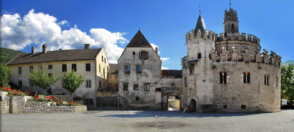 Mittelalterliche Burganlage mit Türmen und Zinnen unter blauem Himmel.