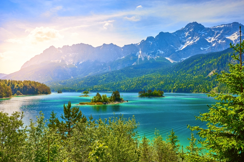 Berglandschaft mit türkisblauem See und bewaldeten Inseln im Sonnenlicht.