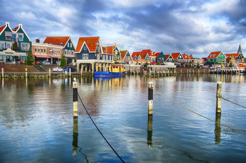 Hafen mit bunten Häusern und Boot, unter bewölktem Himmel.