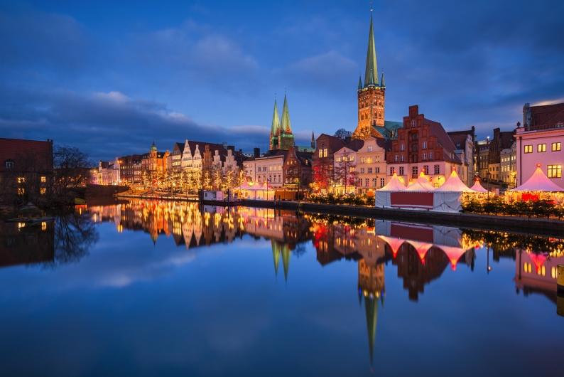 Altstadt mit beleuchtetem Weihnachtsmarkt am Flussufer bei Abenddämmerung.