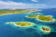 Luftaufnahme von kleinen, grünen Inseln im blauen Meer mit einigen Segelbooten.