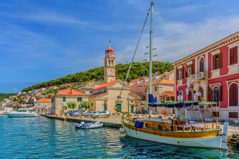 Segelboot in einem malerischen Hafen mit historischen Gebäuden im Hintergrund.