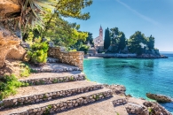Steintreppe führt zu einer Kirche an einer sonnigen Küste mit klarem blauem Wasser.