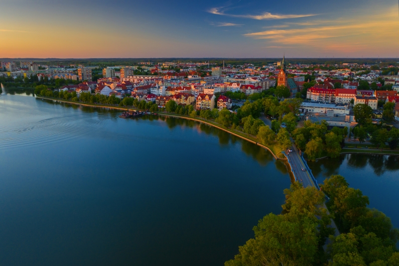 Stadtansicht mit See im Vordergrund bei Sonnenuntergang.