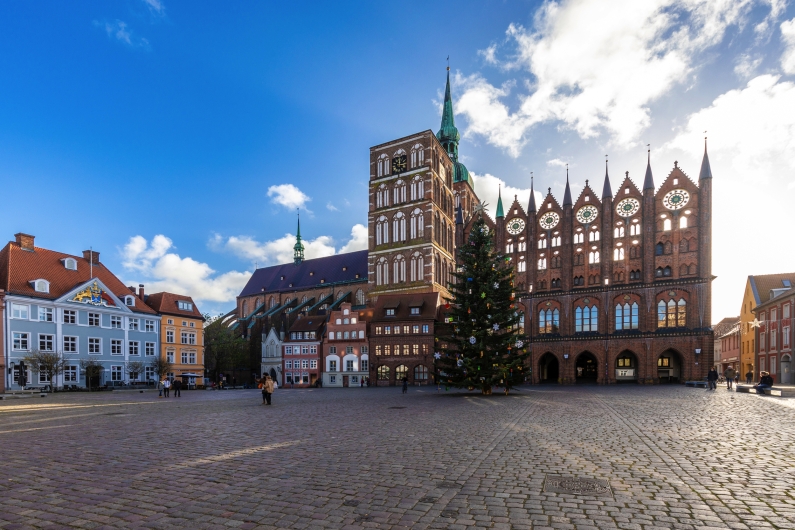 Marktplatz mit historischem Gebäude und Weihnachtsbaum bei klarem Himmel.