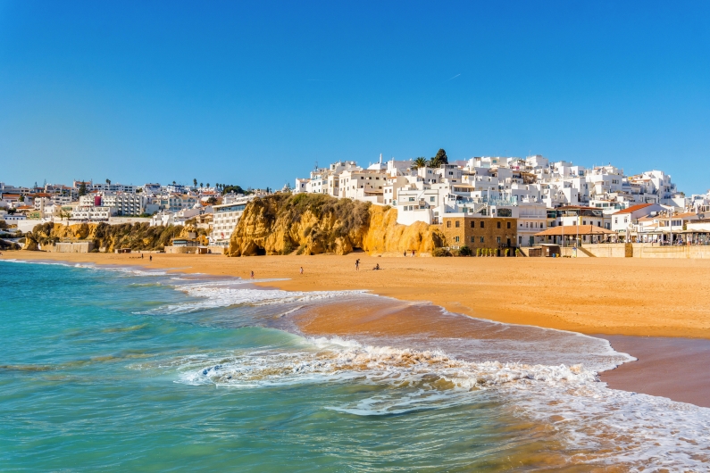 Sandstrand vor der weißen Stadt Albufeira an der Algarve in Portugal mit Felsen im Hintergrund.