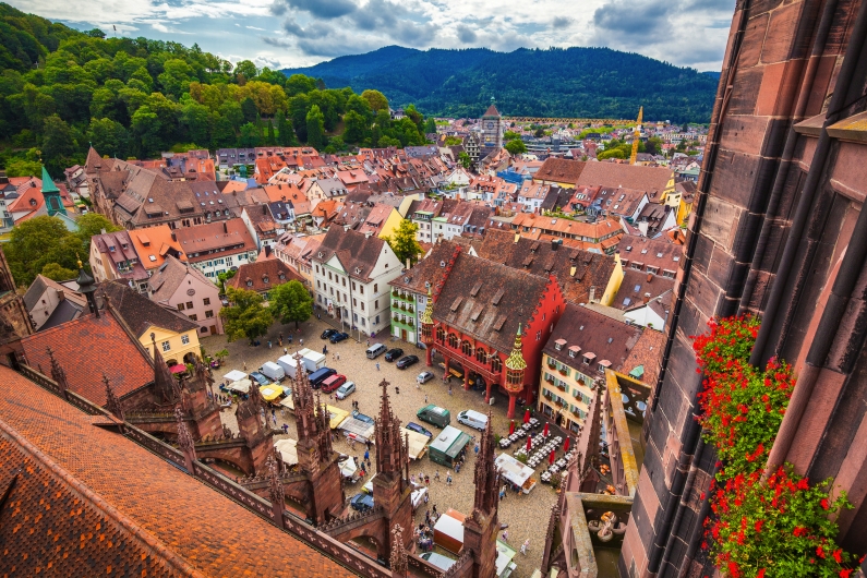 Blick auf bunte Gebäude und Marktplatz in einer Altstadt, umgeben von Hügeln.