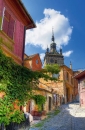 Gasse in einer Altstadt mit Turm und historischen Gebäuden im Hintergrund.