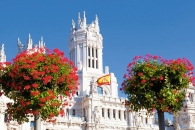 Palacio de Cibeles in Madrid mit spanischer Flagge und Blumen im Vordergrund.