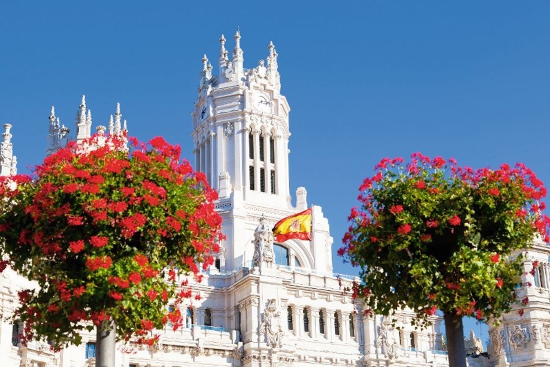 Palacio de Cibeles in Madrid mit spanischer Flagge und Blumen im Vordergrund.
